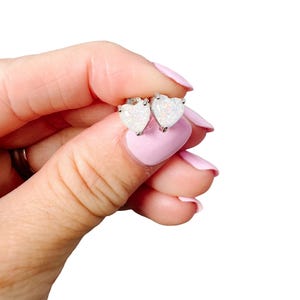 Könnte beinhalten: Ein Paar silberne herzförmige Ohrringe mit weißen Opal-Steinen.