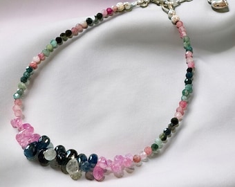 Puede incluir: Un delicado brazalete hecho con pequeñas piedras preciosas facetadas en tonos de rosa, verde y azul. El brazalete tiene un cierre de plata y está dispuesto en un patrón de degradado.