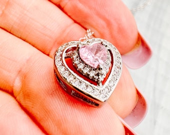 Peut inclure: Un collier avec un pendentif en forme de cœur argenté orné d'un cristal rose au centre. Le pendentif a un design en double cœur avec de plus petits cristaux entourant le plus grand cristal.