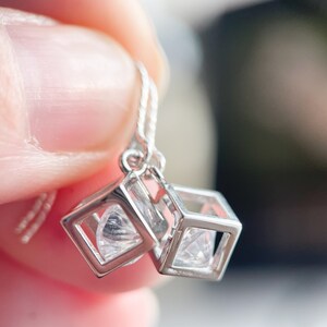 May include: Silver earrings with a cubic zirconia stone in a cube-shaped setting.