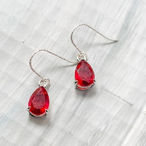 Op de afbeelding: Een paar zilveren oorhangers met rode edelstenen in druppelvorm.