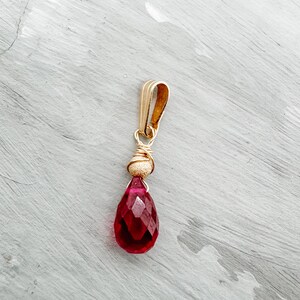 Peut inclure: Un pendentif en forme de larme en pierre rouge avec un enroulement de fil d'or et une bélière en or.