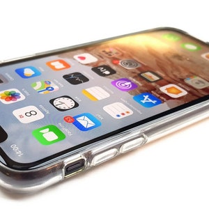 Puede incluir: Una funda transparente para tel&eacute;fono con un iPhone negro en su interior. La pantalla del tel&eacute;fono muestra una variedad de iconos de aplicaciones, incluyendo las aplicaciones de c&aacute;mara, reloj y correo. La hora en el tel&eacute;fono es las 14:00.