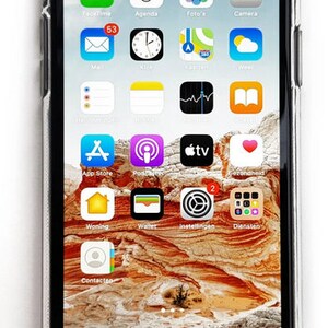 Pode incluir: Um smartphone com uma capa transparente exibe uma tela inicial com v&aacute;rios &iacute;cones de aplicativos. O fundo &eacute; uma paisagem texturizada. A hora &eacute; 14:00 e o telefone mostra um sinal 4G.