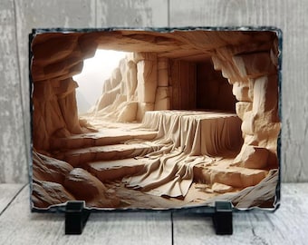 May include: A photograph of a stone cave with a white cloth draped over a stone platform. The cave is lit by a bright light coming from the opening. The stone walls are rough and textured.