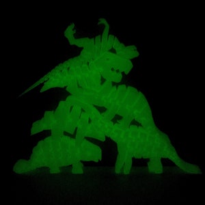 May include: A group of green glow-in-the-dark dinosaur figurines stacked on top of each other. The dinosaurs are in various poses, including standing, sitting, and lying down.