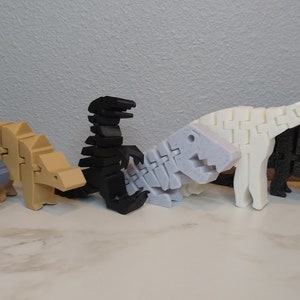 May include: Five articulated dinosaur toys made of plastic. The dinosaurs are in a row from left to right: a blue ankylosaurus, a tan ankylosaurus, a black tyrannosaurus rex, a white stegosaurus, and a black triceratops.