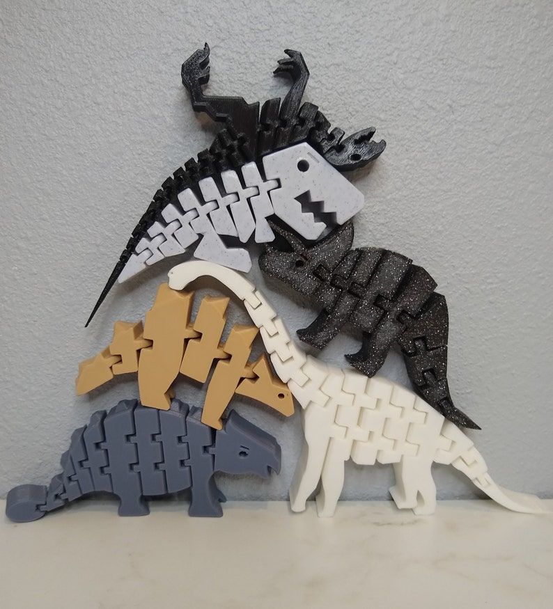 May include: Five articulated dinosaur skeletons made of plastic. The dinosaurs are in various poses and are made of black, white, gray, and brown plastic.