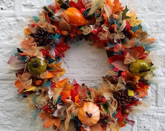 May include: A fall-themed wreath with orange, red, and brown leaves, green gourds, and brown pinecones. The wreath is decorated with brown, gold, and teal tulle.