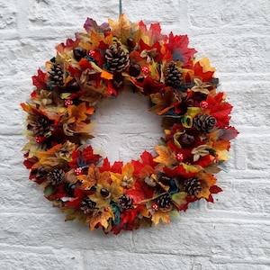 Könnte beinhalten: Ein Herbstkranz mit roten, orangefarbenen und gelben Blättern, Tannenzapfen und Beeren.