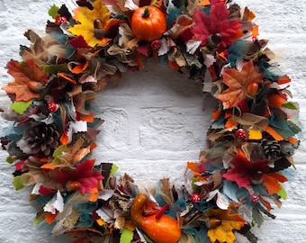May include: A fall-themed wreath made of burlap, fabric scraps, and faux leaves in shades of brown, orange, red, and green. The wreath is decorated with small pumpkins, pinecones, and acorns.