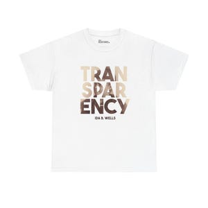 Puede incluir: Camiseta blanca con la palabra "TRANSPARENCY" en un degradado de color beige y marrón. El texto "IDA B. WELLS" está impreso debajo de la palabra. La camiseta también tiene el texto "RESISTANCE" impreso en el cuello.