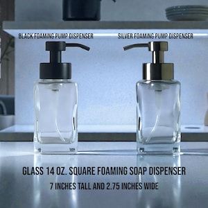 May include: Two clear glass foaming soap dispensers, one with a black pump and the other with a silver pump. The dispensers are square, 7 inches tall and 2.75 inches wide. The text on the image reads: "GLASS 14 OZ. SQUARE FOAMING SOAP DISPENSER".