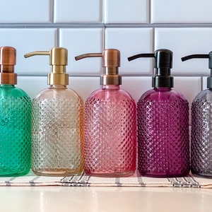 May include: Six glass soap dispensers with textured surfaces and different colored glass. The dispensers have metal pumps in various colors, including copper, gold, and black.
