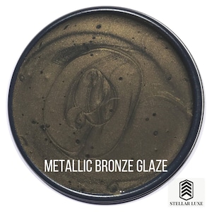 May include: A round container of metallic bronze glaze. The glaze has a swirling, textured appearance. The container is labeled "Metallic Bronze Glaze".