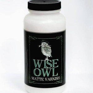 May include: A white bottle with a black lid and a black and white label. The label features an illustration of an owl with a paintbrush in its beak and the text "WISE OWL MATTE VARNISH".