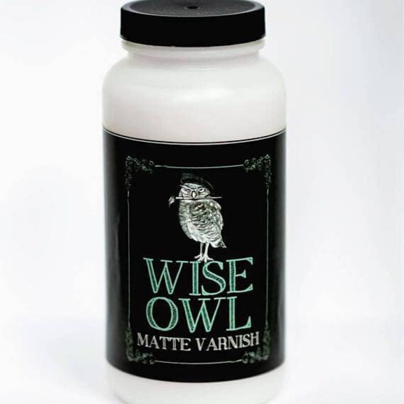 May include: A white bottle with a black lid and a black and white label. The label features an illustration of an owl with a paintbrush in its beak and the text "WISE OWL MATTE VARNISH".