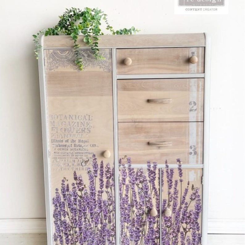 K&ouml;nnte beinhalten: Ein Holzschr&auml;nkchen mit vier Schubladen und zwei T&uuml;ren. Der Schrank ist wei&szlig; lackiert und hat eine Used-Look-Oberfl&auml;che. Die T&uuml;ren sind mit einem Lavendel-Blumenmuster und dem Text "BOTANICAL MAGAZINE FLOWERS PHANTWOR" verziert.