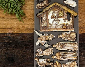May include: A gray silicone mold for crafting, featuring a Holy Night Nativity scene. The mold includes a stable, angels, and figures. The packaging reads "Decor Moulds" and "Holy Night Nativity". The mold is designed for creating decorative elements.
