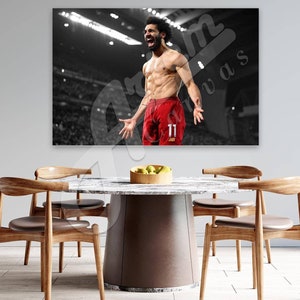 May include: Black and white photo of a soccer player celebrating a goal. The player is wearing red shorts with the number 11 on them. The player is shirtless and has a determined expression on his face.