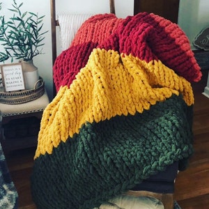 May include: A chunky knit throw blanket with stripes of red, yellow, and green yarn.