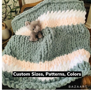 May include: A soft, chunky knit blanket in a light green color with stripes of white and pink. The blanket is draped over a chair and a small gray elephant plush toy is sitting on top of it. The text "Custom Sizes, Patterns, Colors" is printed at the bottom of the image. The text "BAZAART" is printed in the bottom right corner.