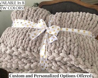 May include: A chunky knit throw blanket in a light beige color, tied with a white ribbon with gold polka dots. The text "AVAILABLE In 8 NEW COLORS" is visible at the top of the image. The text "Custom and Personalized Options Offered" is visible at the bottom of the image.