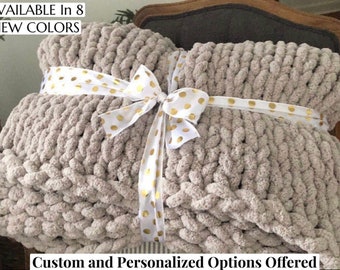 May include: A chunky knit throw blanket in a light beige color, tied with a white ribbon with gold polka dots. The text "AVAILABLE In 8 NEW COLORS" is visible at the top of the image. The text "Custom and Personalized Options Offered" is visible at the bottom of the image.