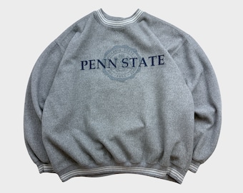May include: A gray sweatshirt with a white and navy blue striped crew neck and cuffs. The sweatshirt has a navy blue embroidered logo that says "Penn State" with a seal.