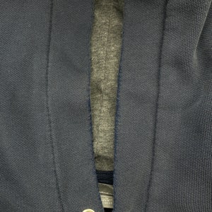 May include: Close-up of a dark blue hooded sweatshirt with a zipper closure. The sweatshirt has a gray lining and two metal eyelets near the bottom.