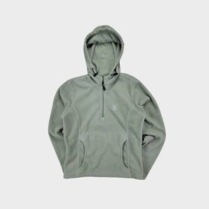 Peut inclure: Un sweat à capuche en polaire vert clair avec une fermeture éclair à moitié et un petit logo sur la poitrine. Le sweat-shirt a une poche kangourou et une capuche à cordon.