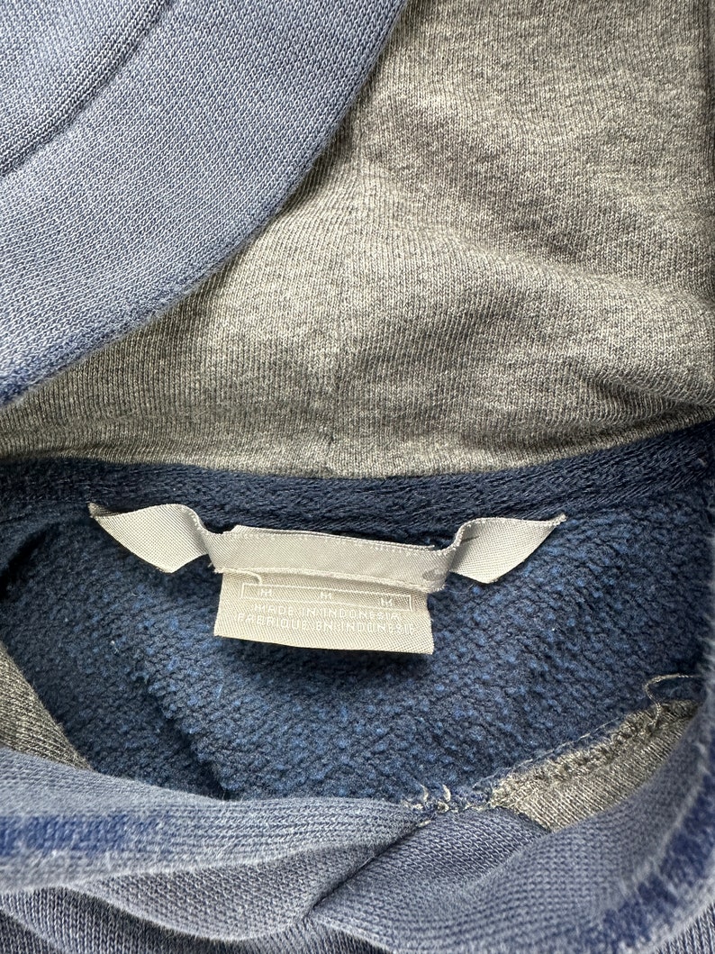 May include: A blue and gray hooded sweatshirt with a white tag that reads "M" and "Made in Indonesia" with a size tag that reads "M".
