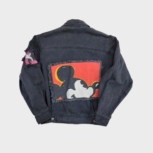 May include: Black denim jacket with a Mickey Mouse graphic patch on the back. The patch is red, yellow, black, and white. The jacket has frayed edges.
