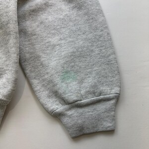 May include: A gray sweatshirt with a ribbed cuff. The sweatshirt has a small, light green stain on the sleeve.