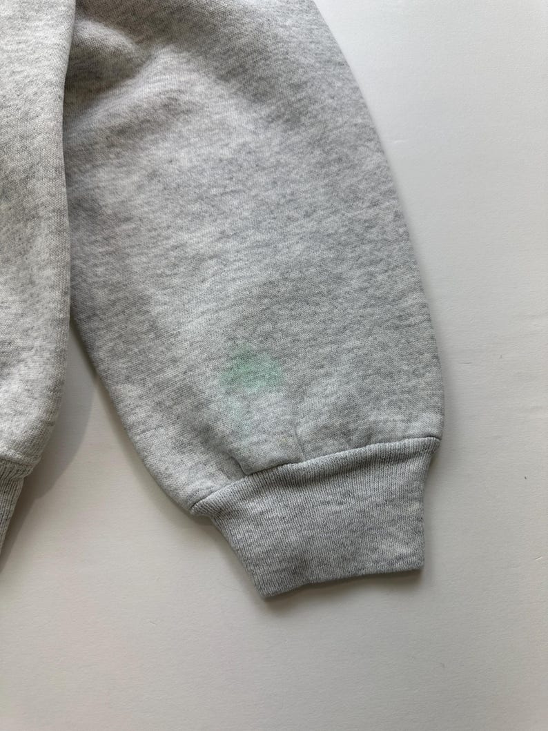 May include: A gray sweatshirt with a ribbed cuff. The sweatshirt has a small, light green stain on the sleeve.
