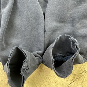 May include: A pair of gray sweatshirt cuffs with frayed edges. The cuffs are turned inside out, revealing a soft, dark gray lining.