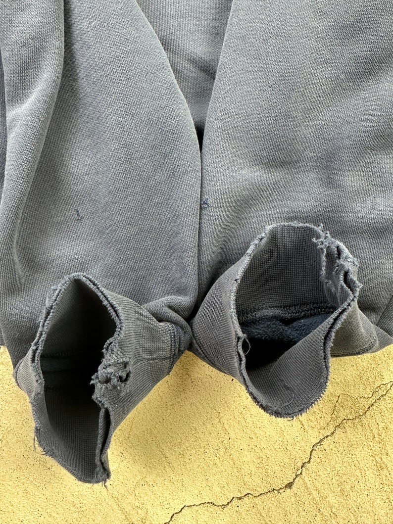 May include: A pair of gray sweatshirt cuffs with frayed edges. The cuffs are turned inside out, revealing a soft, dark gray lining.