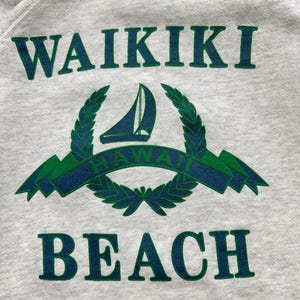 May include: A gray sweatshirt with a green and blue graphic print that says "WAIKIKI BEACH" with a sailboat and a laurel wreath.