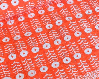 May include: A bright orange quilted blanket featuring a repeating white pattern of stylized floral motifs and vertical lines. The fabric has a visible stitched texture throughout, with a distinct striped border along the bottom edge of the textile.