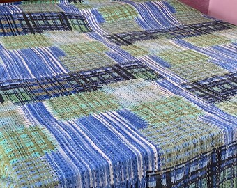Könnte beinhalten: Ein Bett mit einer blau, grün und schwarz gemusterten Steppdecke. Die Steppdecke hat ein Patchwork-Design mit vertikalen und horizontalen Linien. Das dunkelbraune Kopfteil hat goldene Akzente und das Hindi-Wort "स्वागतम".