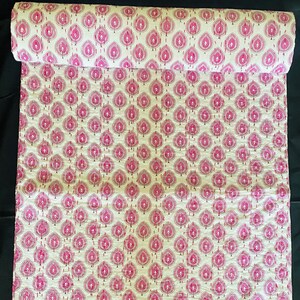 May include: A rolled-up fabric with a repeating pattern of pink leaf-like shapes on a cream background. The leaves are outlined with a darker pink stitch, creating a textured effect. The fabric is likely cotton or a similar material.