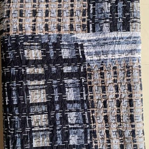 May include: A folded quilt with a geometric pattern in shades of blue, gray, and tan. The design features a grid-like arrangement with white stitching, creating a textured appearance. The quilt's color palette and pattern suggest a modern aesthetic.
