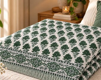 May include: A folded quilt featuring a white base with a repeating dark green botanical print of stylized flowers and leaves. The quilt has a wide decorative border with a floral pattern and thin striped edges, showcasing a quilted texture.