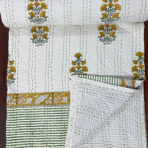 May include: White and yellow floral patterned quilt with green stitching. The quilt features repeating yellow flower bouquets and a green and yellow border. The quilt is folded and rolled up.