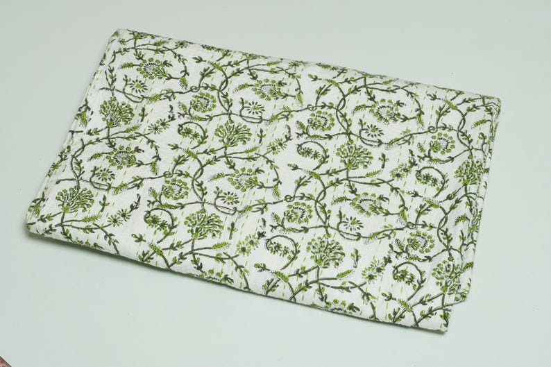 Green floral block print Kantha quilt rolled and unrolled on a white background, soft cotton hand-stitched blanket.