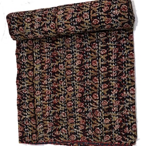 May include: A black kantha quilt with a floral pattern in shades of red, brown, and white. The quilt is rolled up and has a hand-stitched design.