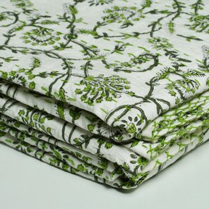 Green floral block print Kantha quilt rolled and unrolled on a white background, soft cotton hand-stitched blanket.