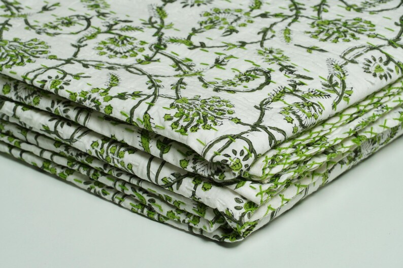 Green floral block print Kantha quilt rolled and unrolled on a white background, soft cotton hand-stitched blanket.