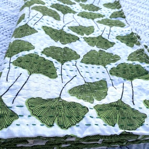 May include: White kantha quilt with a green ginkgo leaf pattern. The quilt is folded in thirds and the fabric is soft and textured.