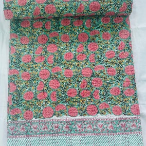 Op de afbeelding: Een groene en roze kantha-deken met een bloemenpatroon. De deken heeft een witte rand met een roze en groen bloemenontwerp.